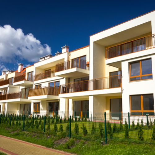 Edificio residencial moderno con balcones y jardín, rodeado de cercado